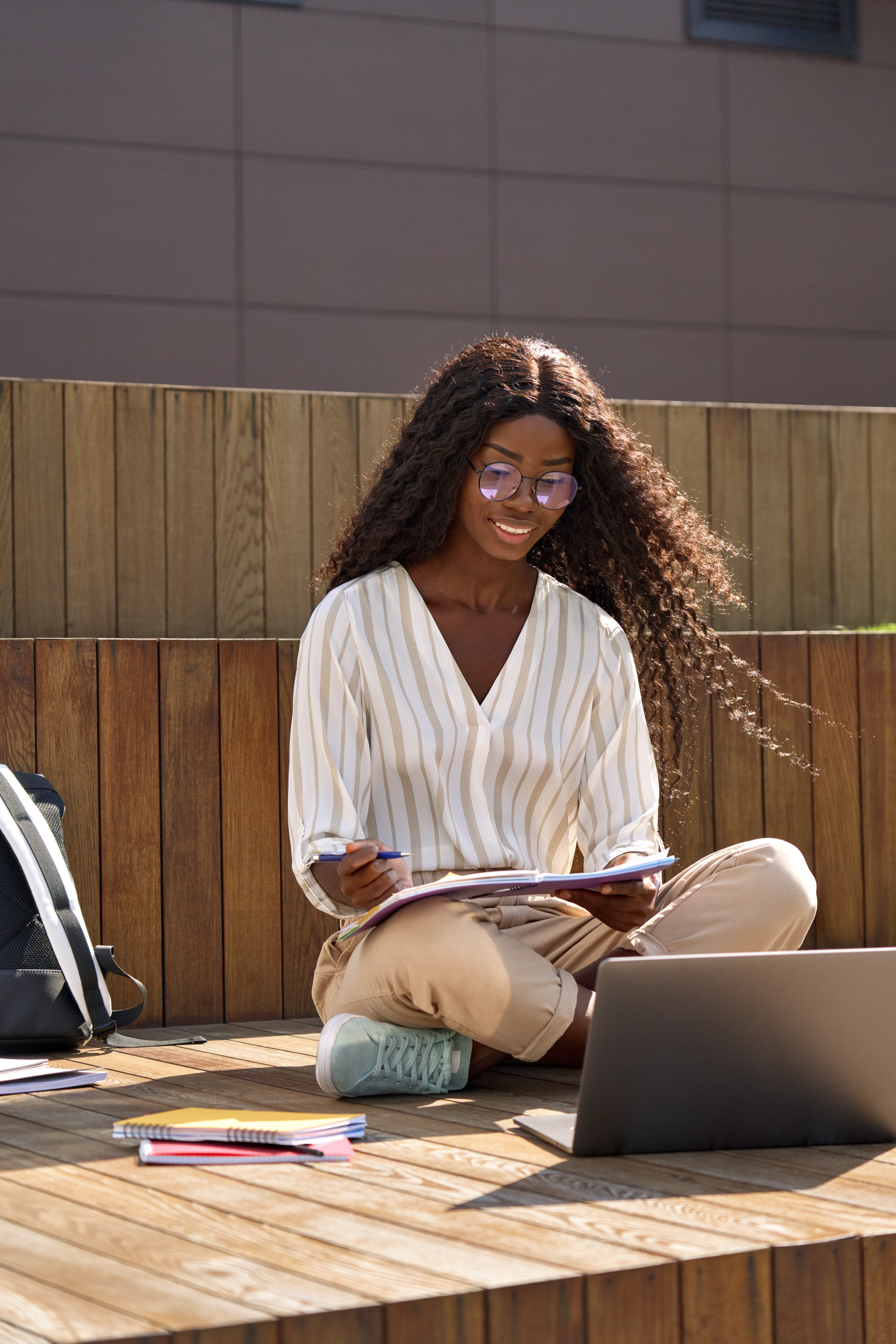 A focused learner studying outdoors with a laptop and notebooks